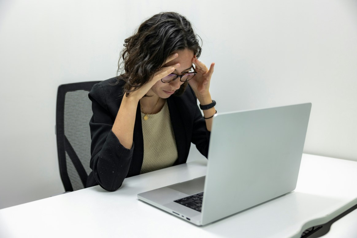 Stressed woman holding head while looking at laptop screen in office.