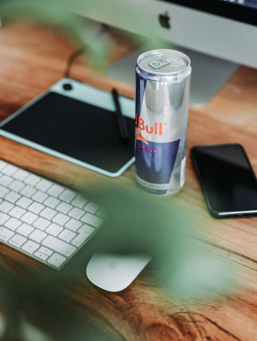 A redbull on a wooden desk next to a keyboard and graphics tablet for designing computer imagery.