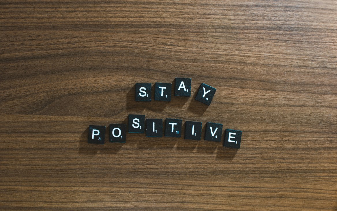 Black letter tiles spelling “Stay Positive” on a wooden surface.