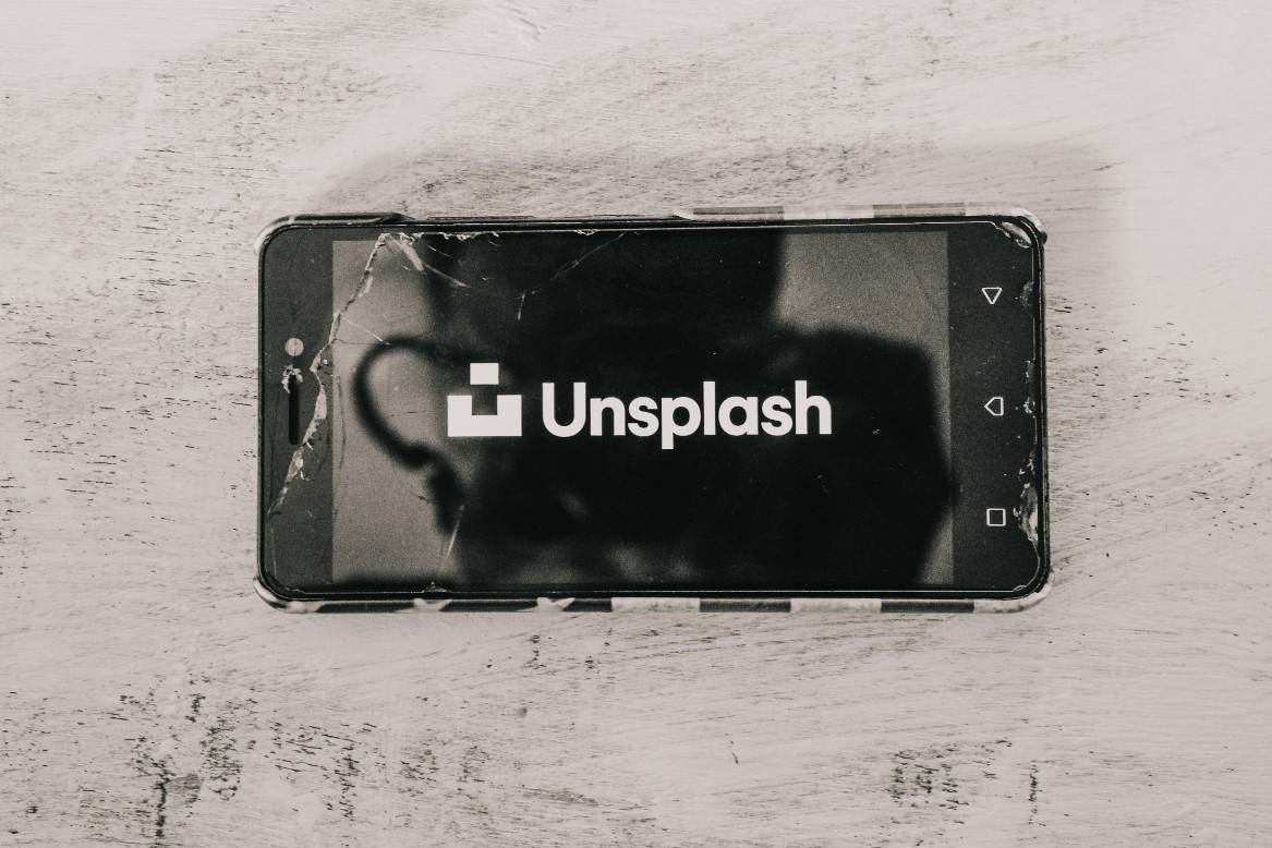 Cracked smartphone screen displaying the Unsplash logo on a wooden surface.