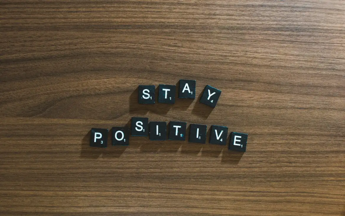 Black letter tiles spelling “Stay Positive” on a wooden surface.